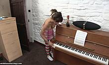 Uma morena de meias listradas tenta se mover para um piano enquanto também está sem blusa