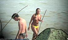Η τόπλες γυναίκα δείχνει το στήθος της σε μια παραλία γυμνιστών